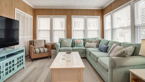 Un salon comprenant un téléviseur, une table basse, un canapé et un fauteuil en osier.