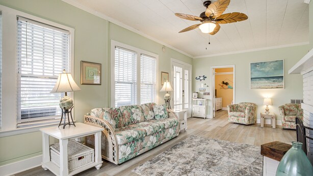 Un salon spacieux avec un canapé, des fauteuils, un ventilateur de plafond et une grande fenêtre.