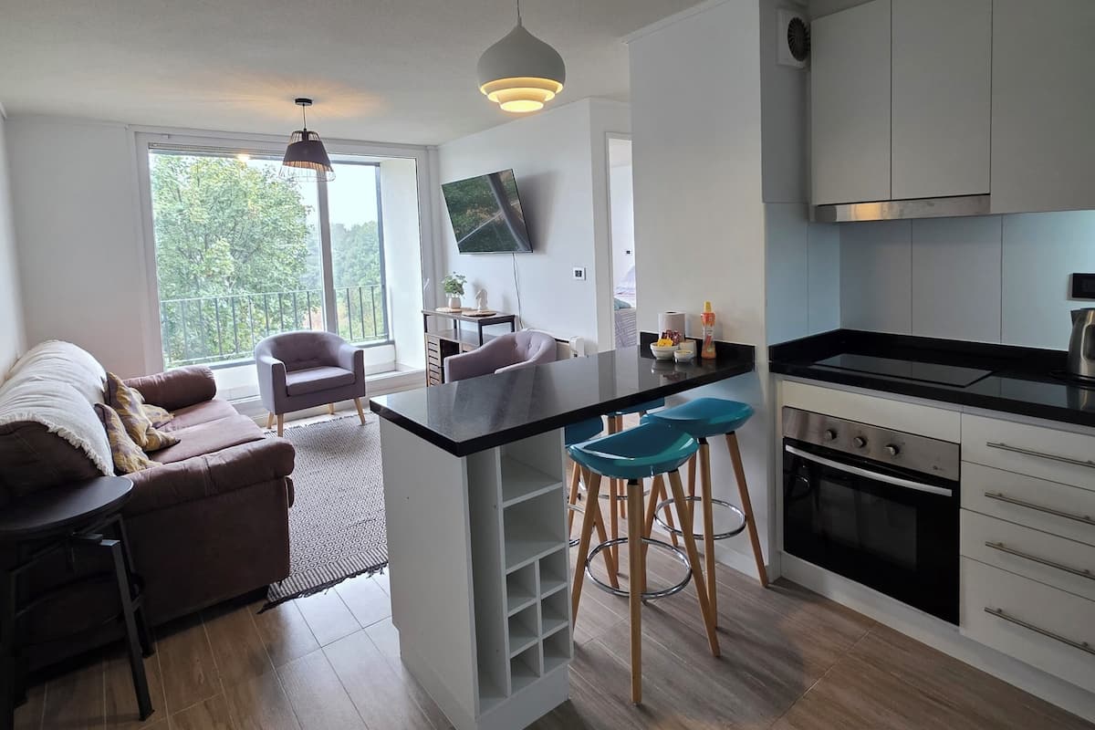 Een moderne keuken met een centraal eiland, barstoelen, een inbouwoven en een flatscreen televisie.