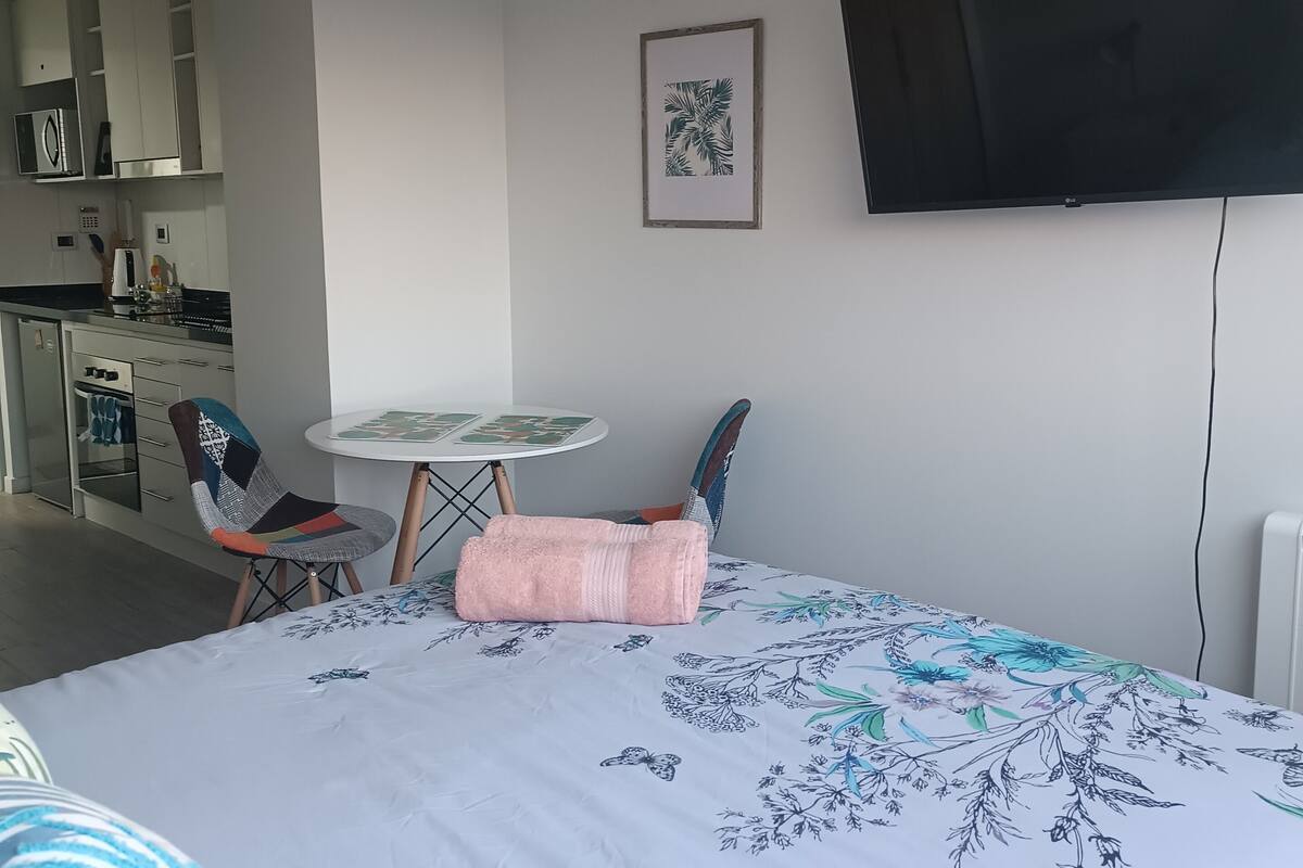 Een slaapkamer met een bed, een televisie aan de muur, een klein tafeltje en een stoel.