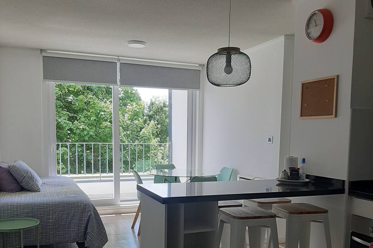 Een moderne keuken met een centraal eiland, witte barkrukken en een eettafel met stoelen.