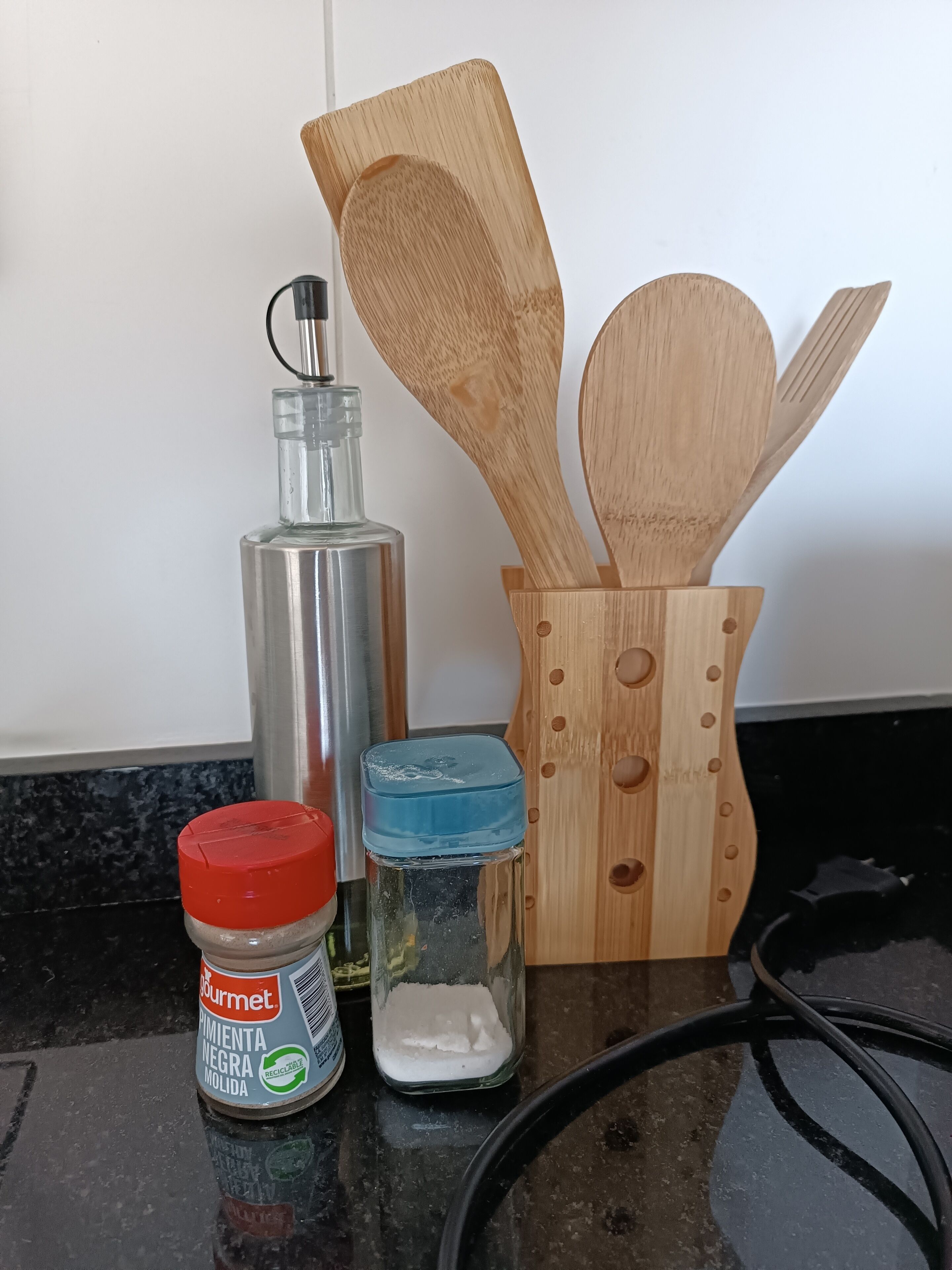 Una encimera de cocina con un frasco de especias, una botella de vidrio, un bote de polvo blanco y utensilios de madera.