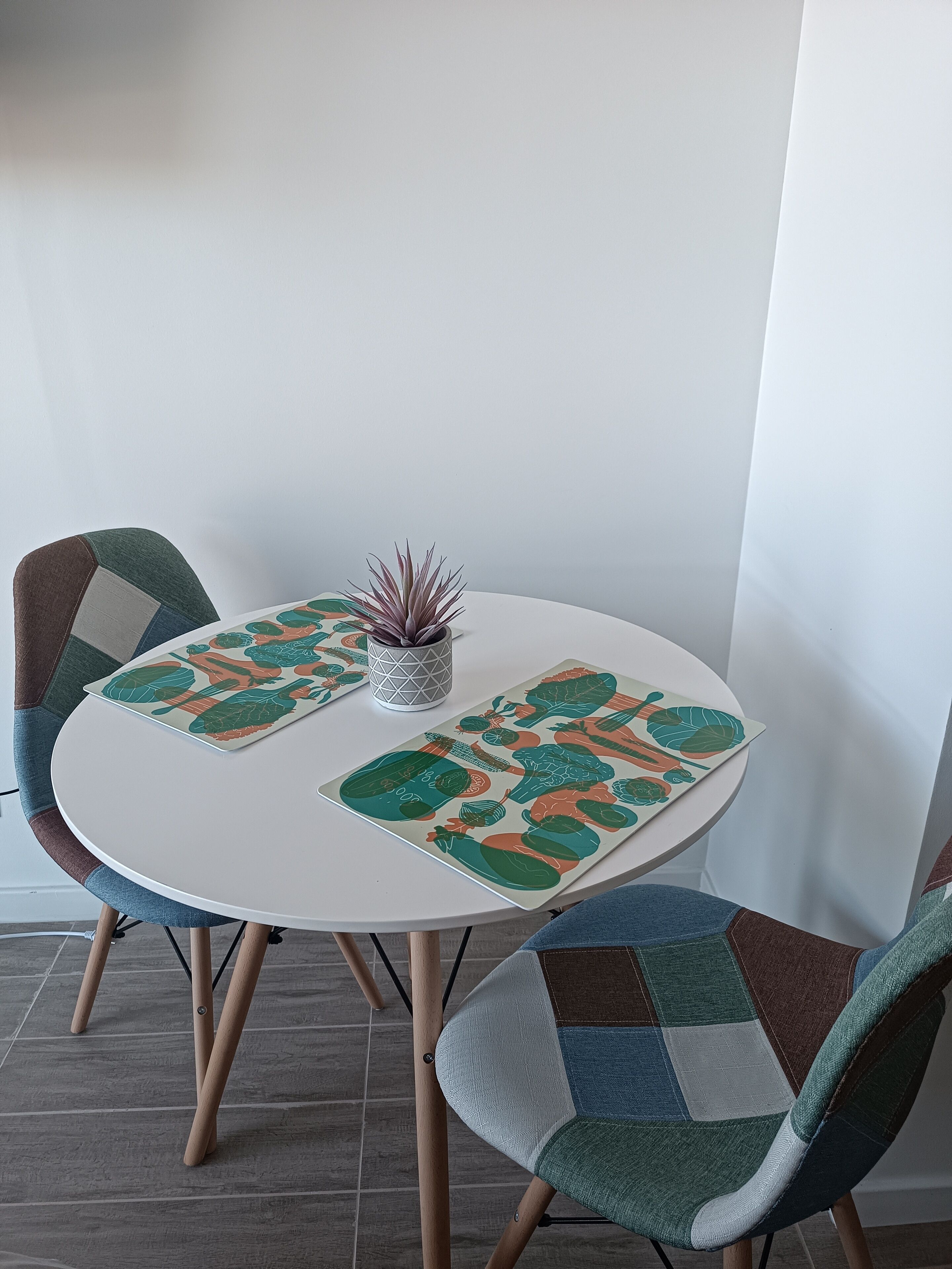 A round table with a white surface, surrounded by four chairs with a patchwork design. A small potted plant is placed on the table.