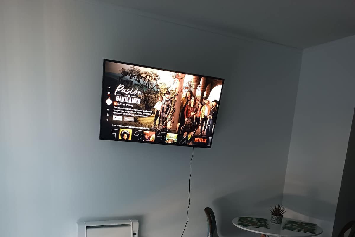 Een hotelkamer met een groot bed, een aan de muur bevestigde televisie, een klein rond tafeltje met stoelen en een radiator op de vloer.