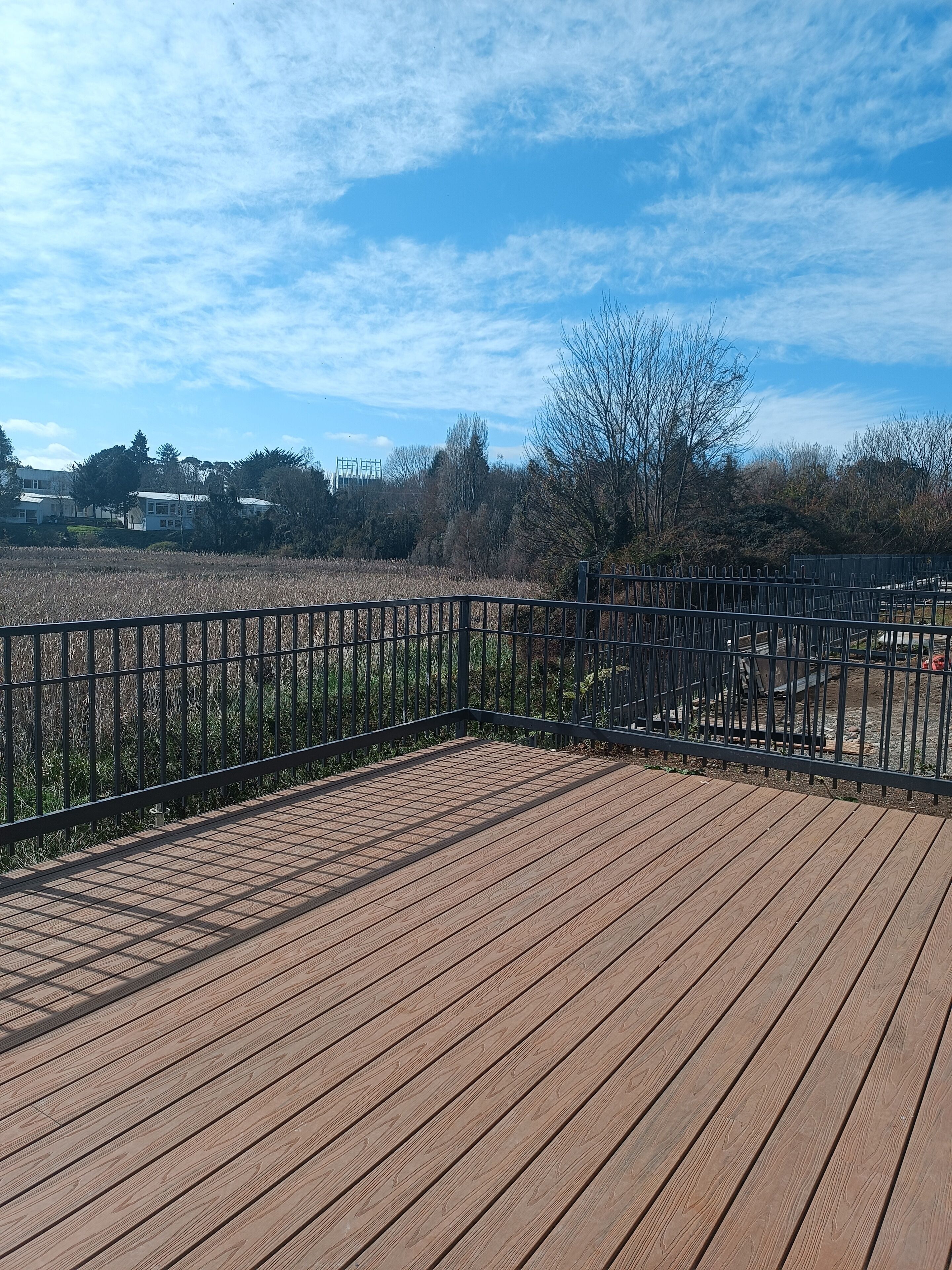 Eine Holzterrasse mit Metallgeländer, die auf ein Feld und Bäume blickt.