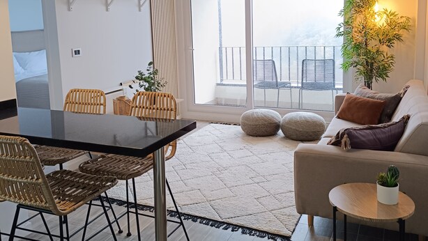 A modern living room with a dining area, large windows, and a balcony.