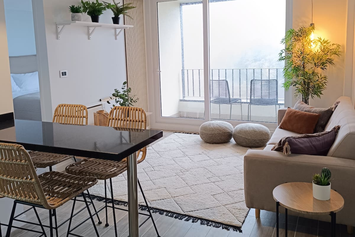 Een moderne woonkamer met een eethoek, grote ramen en een balkon.