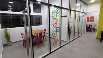 A modern office space with glass partitions, a wooden table with red chairs, and a potted plant.