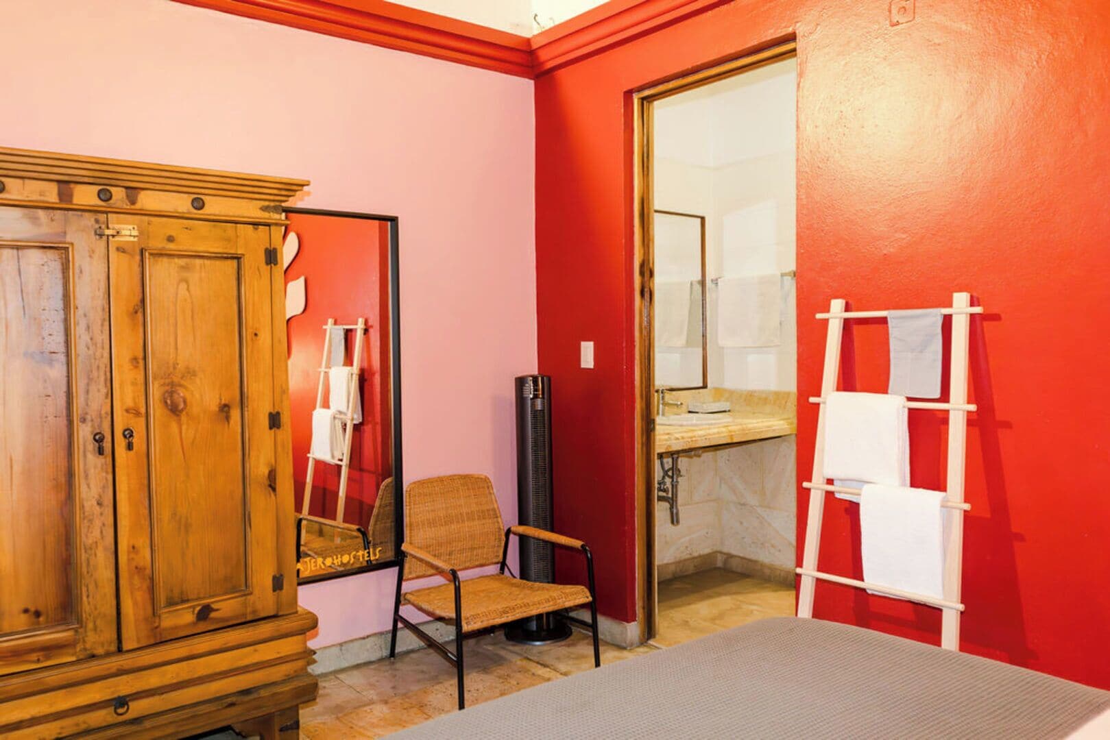 Una habitación con un armario de madera, una silla de mimbre, una mesita pequeña y un perchero blanco.