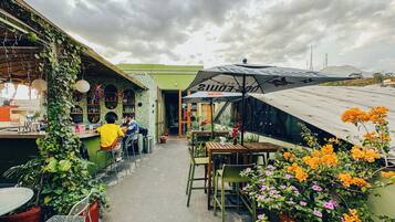 Un café al aire libre con mesas y sillas, una zona de bar y plantas en macetas.