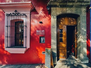 A red building with a barred window, a sign for 'Viajero Hostels' with a rooftop bar, and a wooden door with a flower design. - Viajero Oaxaca Hostel (Oaxaca)