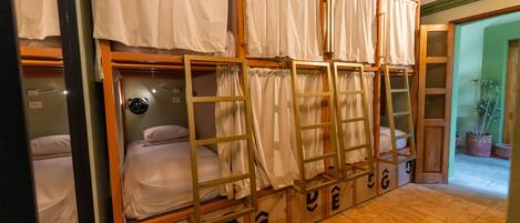 A row of bunk beds with wooden frames and white bedding, each with a small ladder and a storage box underneath.