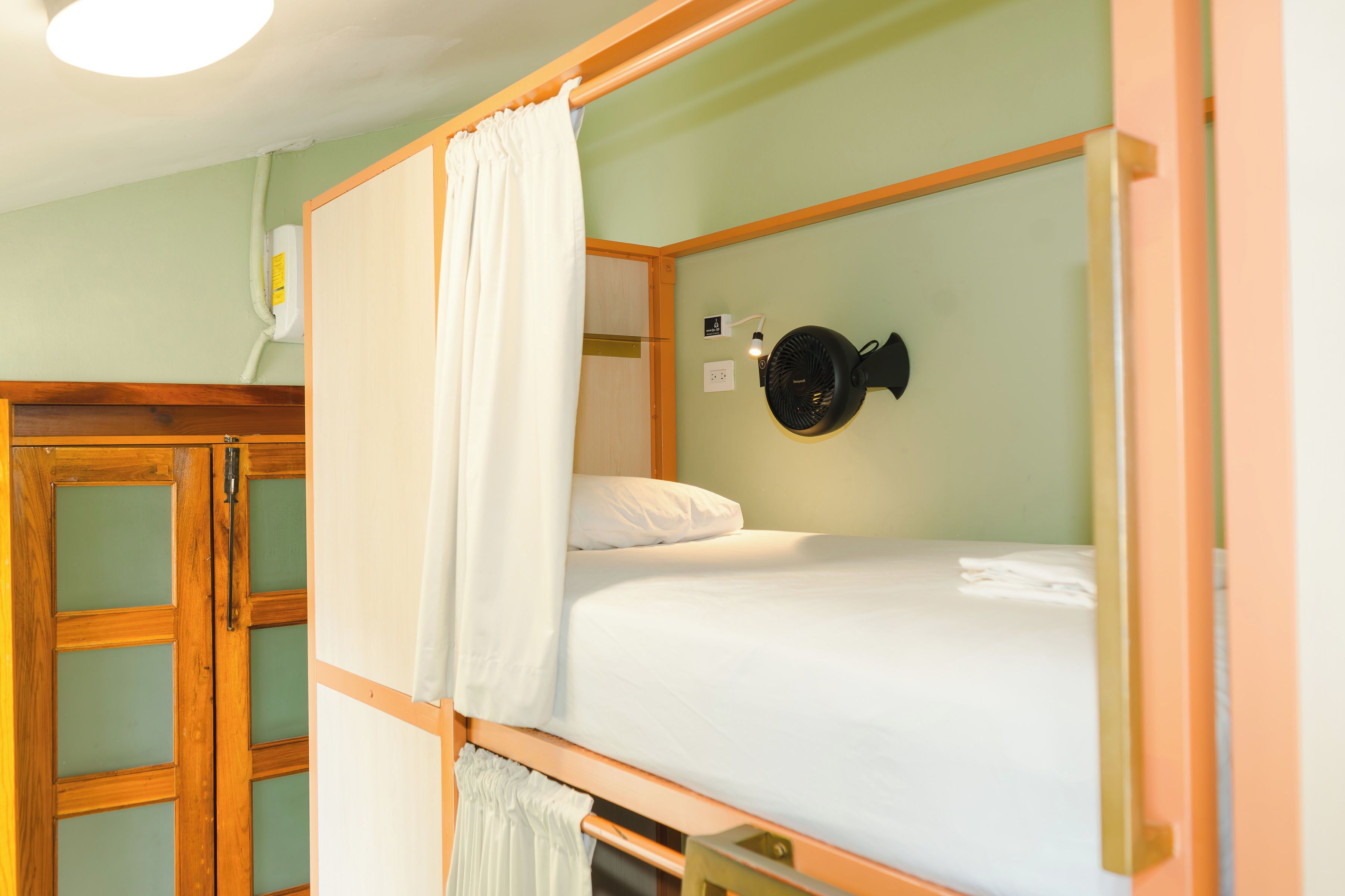 A single bed with a white mattress and a black fan on the wall.
