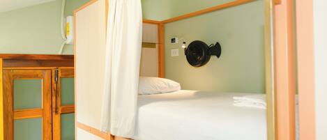 A single bed with a white mattress and a black fan on the wall.