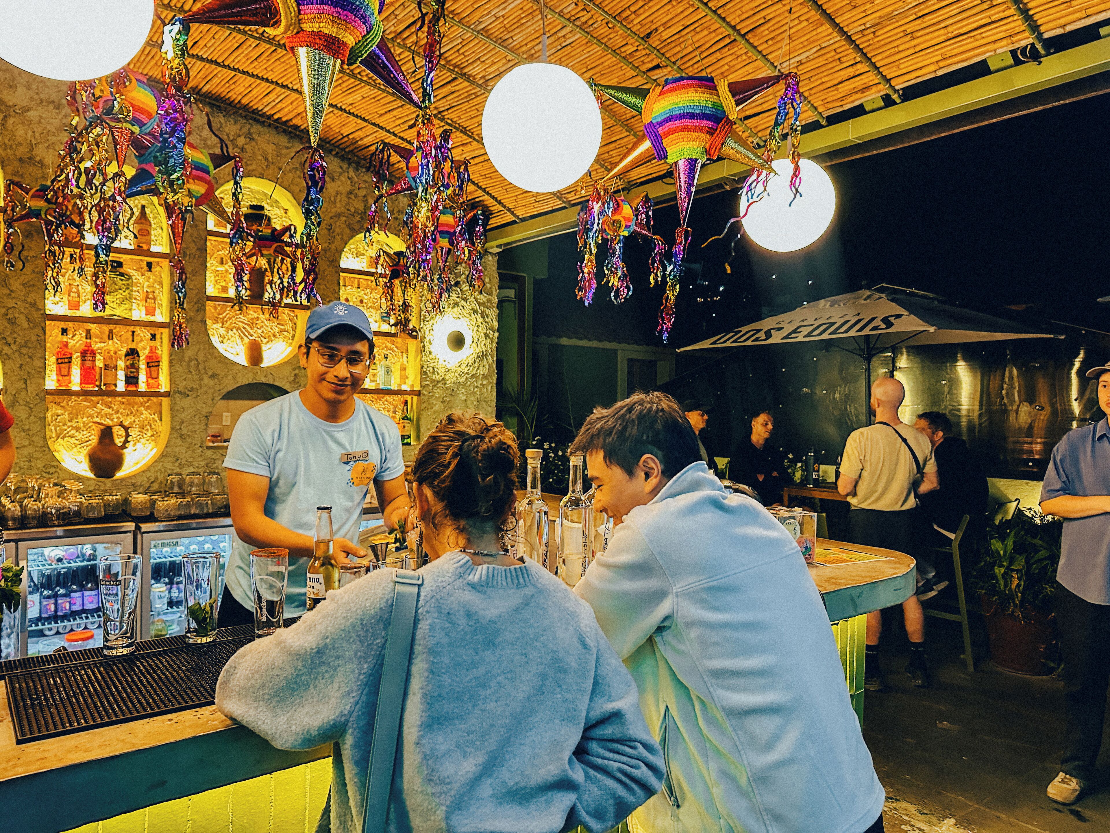 A bar area with a bartender, shelves with bottles, and hanging decorations.