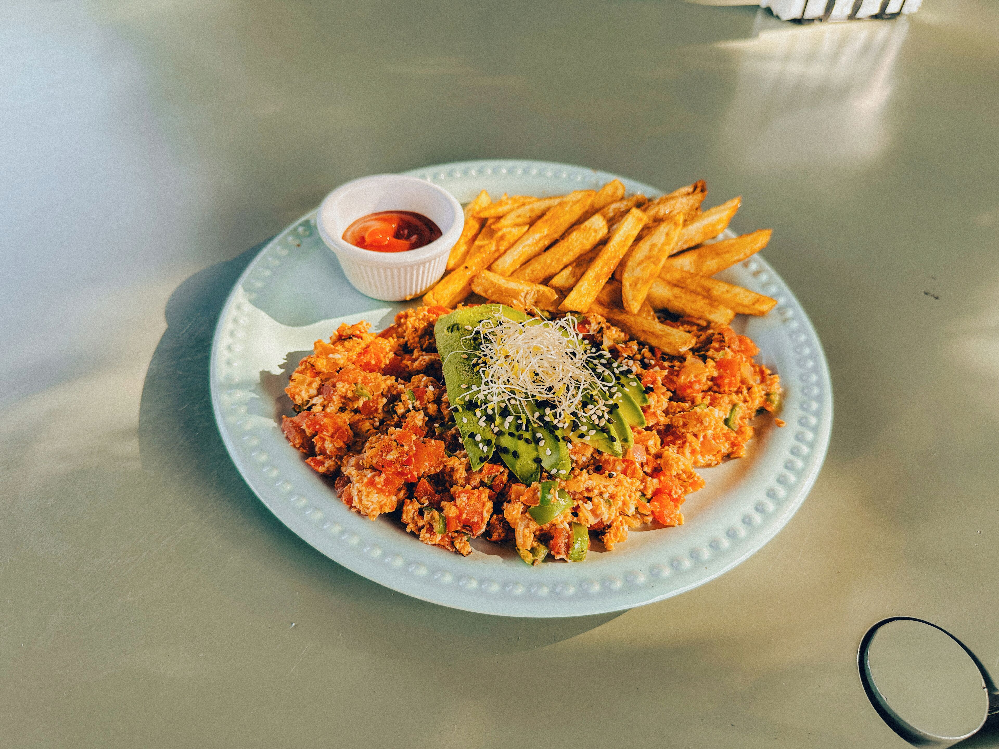 A plate of food with fries and a small bowl of ketchup.