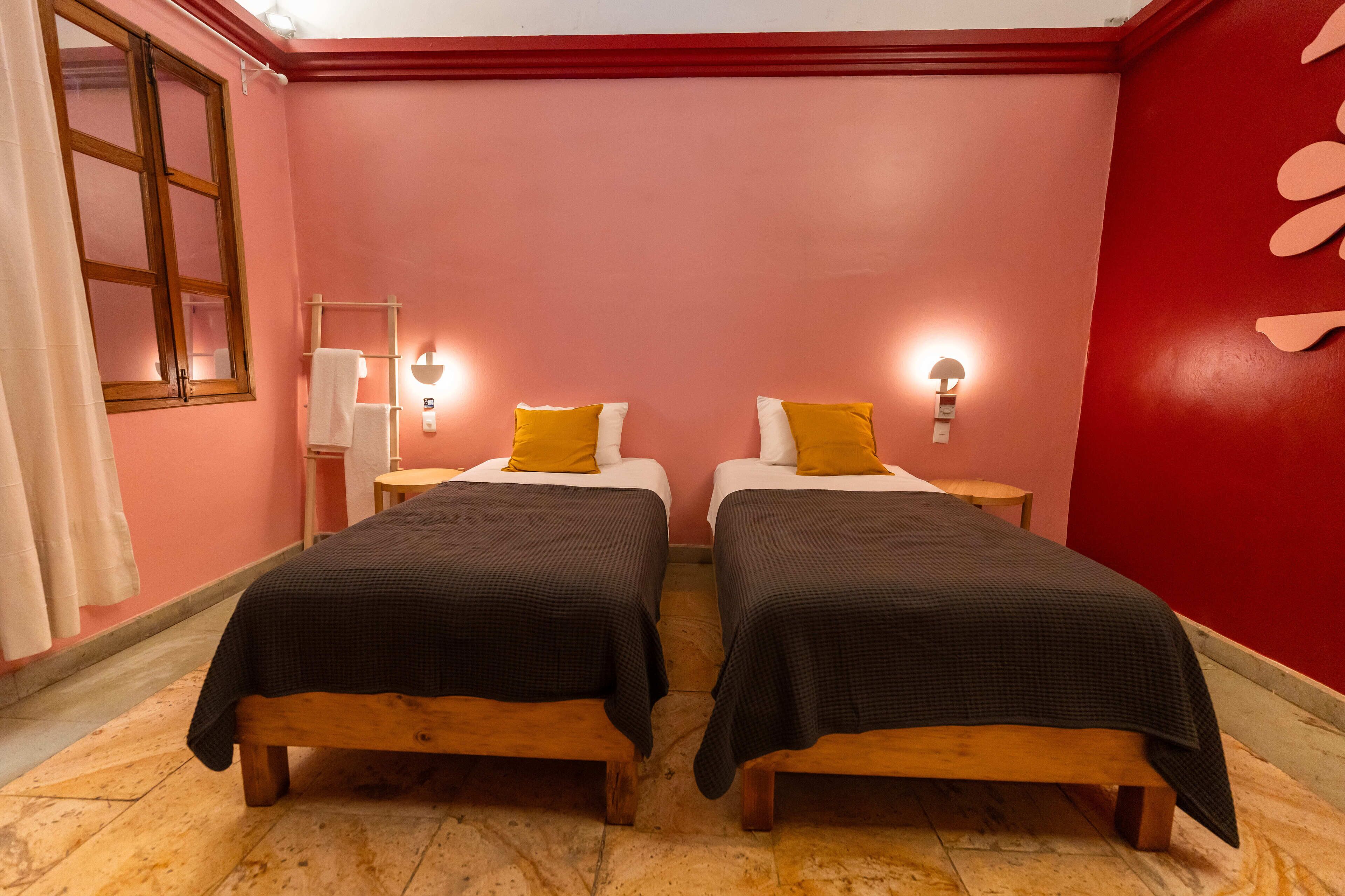 Una habitación con dos camas, cada una con estructura de madera y ropa de cama negra, paredes rosas y suelo de madera.