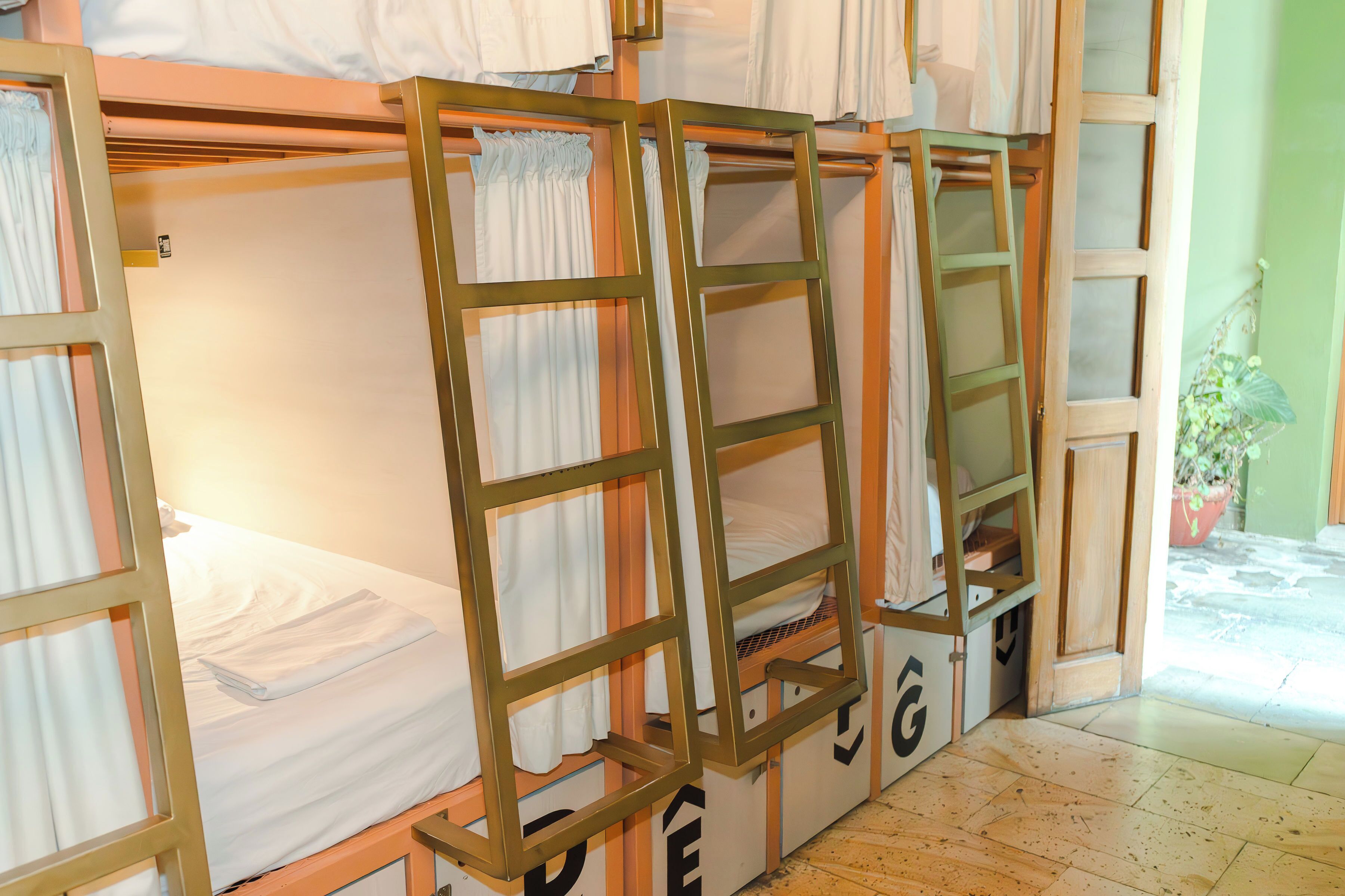 A dormitory-style room with bunk beds, wooden frames, and a small window with curtains.