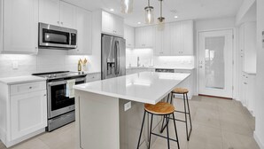A modern kitchen with white cabinetry, stainless steel appliances, a large island with stools, and pendant lighting. - Coastal Cottage-Steps to Siesta Key Beach (Siesta Key)