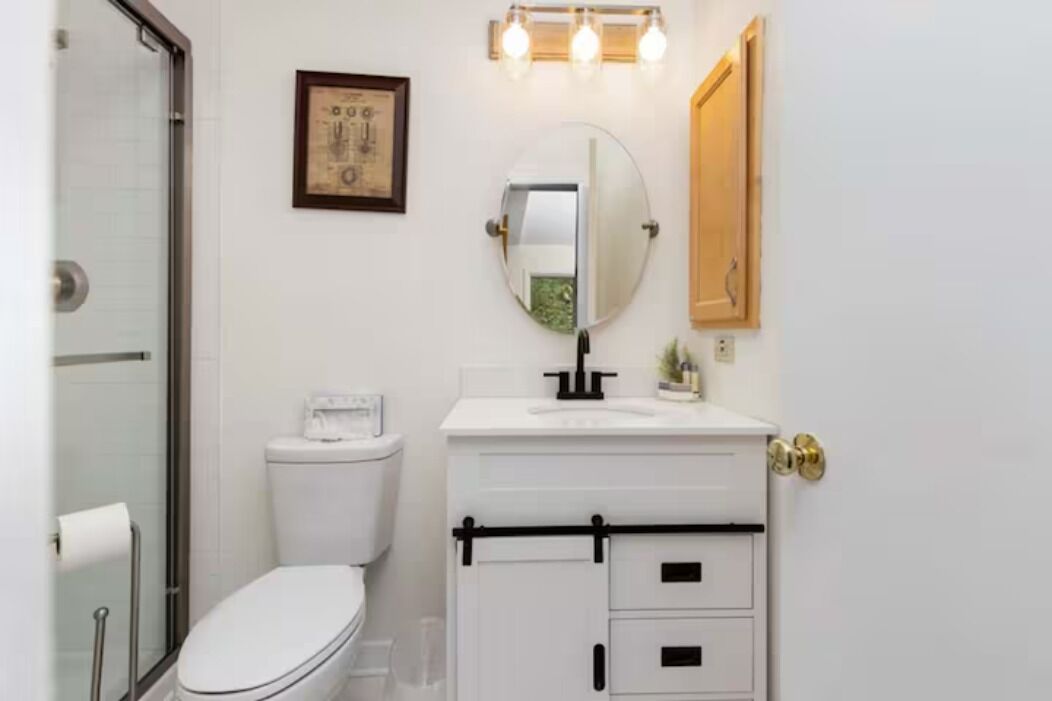 A bathroom with a toilet, a sink with a mirror, and a shower area.