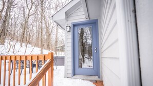 Une terrasse en bois recouverte de neige, une porte bleue et un mur extérieur blanc.