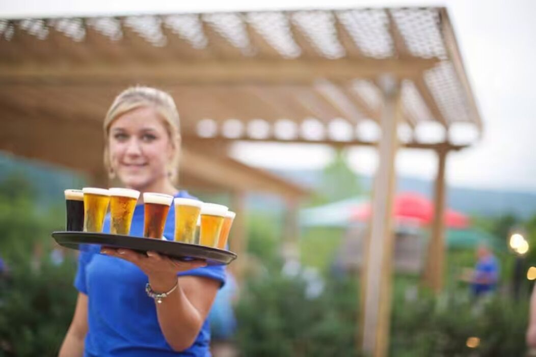 A person holding a tray with multiple beer glasses.