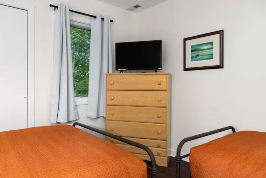 Un dormitorio con dos camas, un aparador de madera, un televisor y una ventana con cortinas.