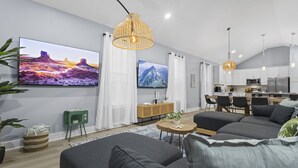 A modern living room with a sofa, a TV, and a dining area with a table and chairs. - Two Amazing Modern & Spacious Beach Retreats, 9 Bedroom, 6 bathrooms (Gulfport)