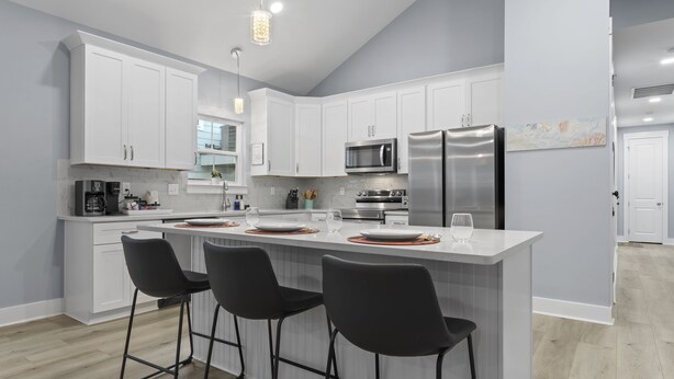 A modern kitchen with white cabinets, stainless steel appliances, and a central island with bar stools. - Two Amazing Modern & Spacious Beach Retreats, 9 Bedroom, 6 bathrooms (Gulfport)