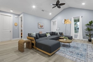 A modern living room with a sectional sofa, a small coffee table, wicker stools, a floor lamp, and a large window with curtains. - Two Amazing Modern & Spacious Beach Retreats, 9 Bedroom, 6 bathrooms (Gulfport)