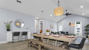 A modern kitchen with a large wooden table, black chairs, and a hanging light fixture. - Two Amazing Modern & Spacious Beach Retreats, 9 Bedroom, 6 bathrooms (Gulfport)