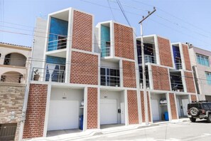 A multi-story building with a modern design, featuring a combination of brick and white exterior walls, and multiple garage doors. - New Townhouse, A/C, secure and great location! (Ensenada)