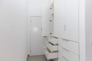 Ein weißer Kleiderschrank mit Schubladen und Türen, eine geschlossene Tür links, und ein Fliesenboden.