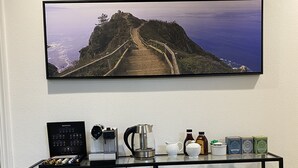 Angolo caffè con macchina da caffè, tazze e condimenti su uno scaffale, con vista panoramica su un sentiero costiero.