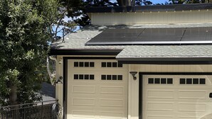 Un garage per due auto con tetto solare, un albero a sinistra e una recinzione in metallo.