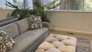Un soggiorno con un divano grigio, un poggiapiedi beige e un tappeto decorato.