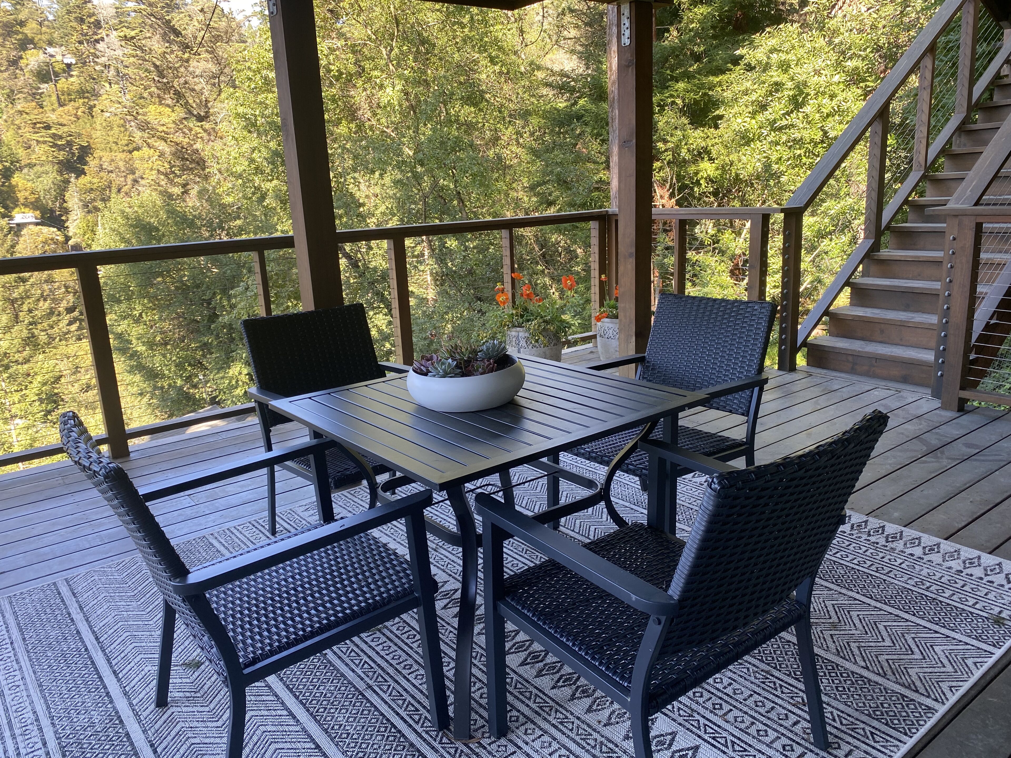 A covered outdoor seating area with a table and chairs, surrounded by a wooden deck and a railing.