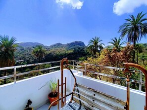A balcony with a view of a mountainous landscape, a wooden chair, and a potted plant. - Charan Villa (Abu Road)
