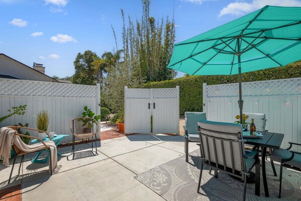 A patio area with a table, chairs, a large umbrella, and a gate. - Comfortable Montecito Studio Cottage Walking Distance to Beach! (Santa Barbara)