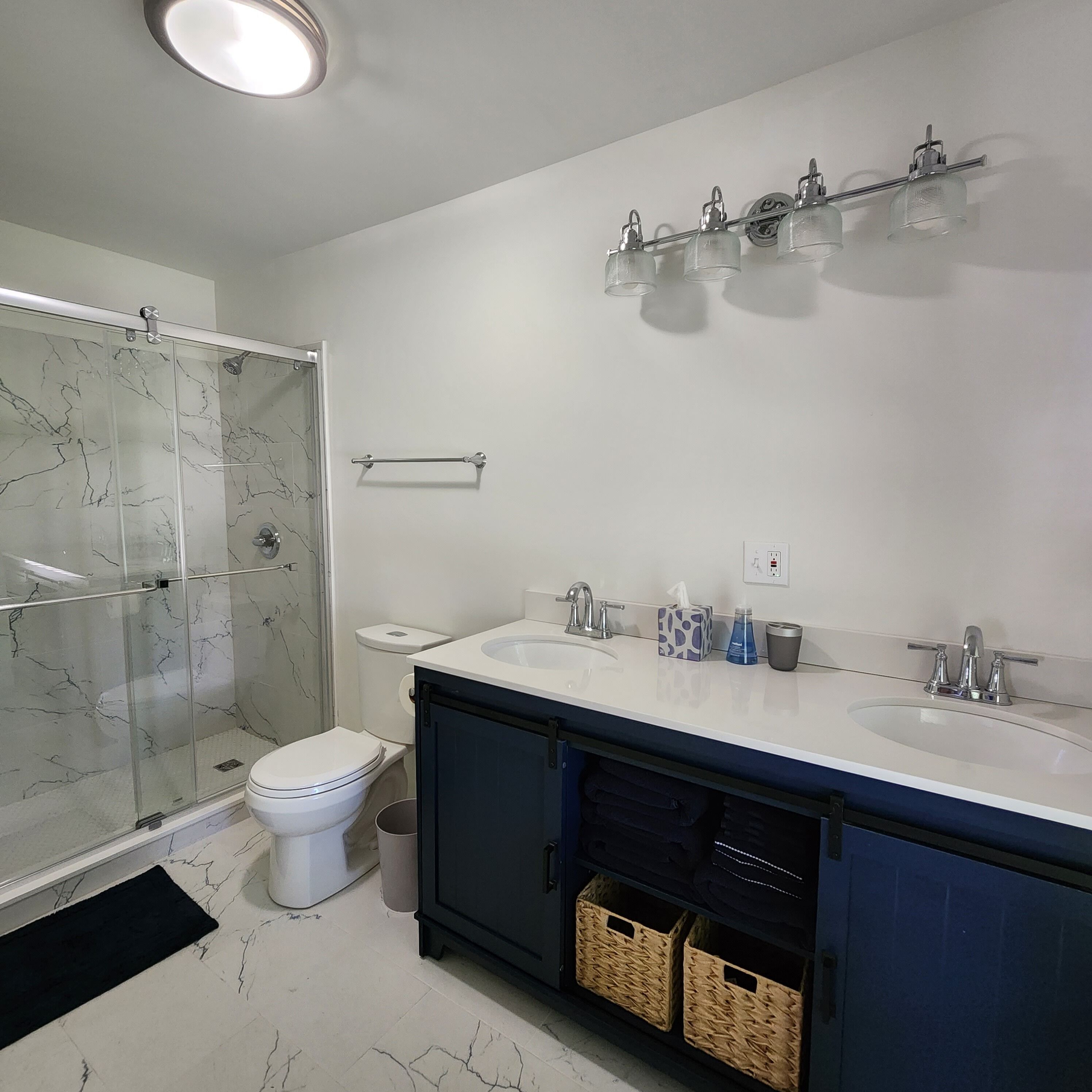 Ein modernes Badezimmer mit Duschkabine aus Glas, Toilette, Waschbecken-Doppelanordnung und Handtuchhalter.