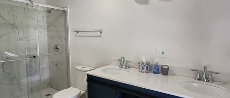 Ein modernes Badezimmer mit Duschkabine aus Glas, Toilette, Waschbecken-Doppelanordnung und Handtuchhalter.