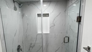 A glass-enclosed shower with a marble floor and a small window.