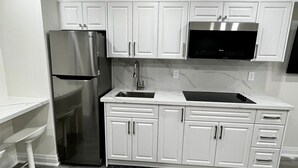 A modern kitchen with white cabinets, a stainless steel refrigerator, a microwave, and a sink.