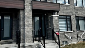 A modern multi-story residential building with a brick facade, large windows, and a front entrance with a black door and steps.