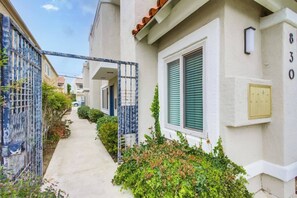 A narrow pathway leading to a residential building with a gated entrance, a mailbox, and a number plaque.