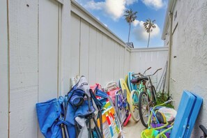 A narrow outdoor space with a white fence, bicycles, and surfboards leaning against it.