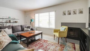 A living room with a sofa, coffee table, and armchair, a fireplace, and a window with blinds. - Pet-friendly 1 block to the beach with parking (San Diego)