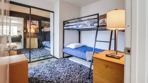 A compact hotel room with a bunk bed, a small desk with a lamp, and a view of a living area through a glass door. - Pet-friendly 1 block to the beach with parking (San Diego)