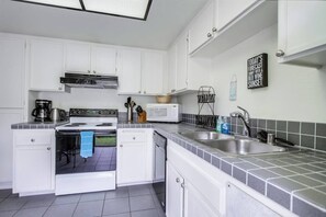 A modern kitchen with white cabinets, a stove, microwave, and a sink.