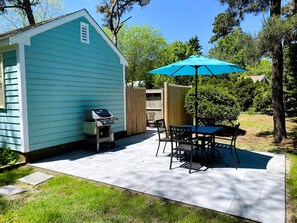 A backyard with a patio, a grill, a table with chairs, and a blue umbrella. - Cozy Cottage in Eastham near National Seashore (Eastham)